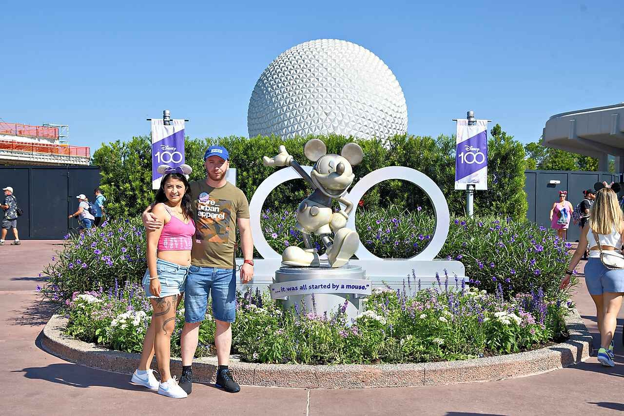 Pareja de viaje en Disney junto a una estatua de Mickey Mouse y la esfera de Epcot